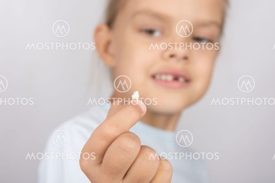 Six year old girl holding a fallen tooth and smiling...