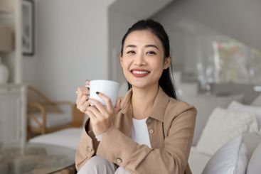 Happy relaxed beautiful young Asian woman drinking...