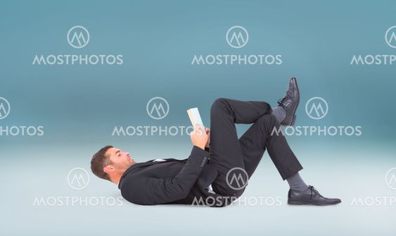 Composite image of businessman lying on the floor reading book