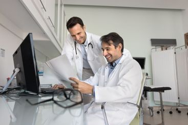 Two happy male doctors reading paper medical report at...