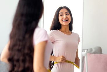 Attractive young Indian woman measuring her waist with...