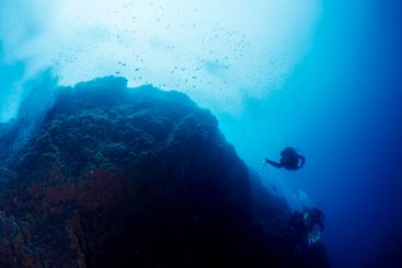 scuba divers diving near of a rocky formation