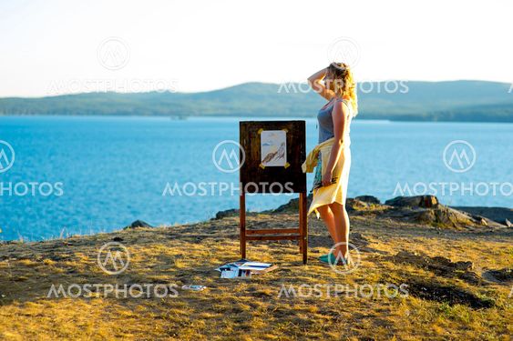 young artist draws a seascape at sunset