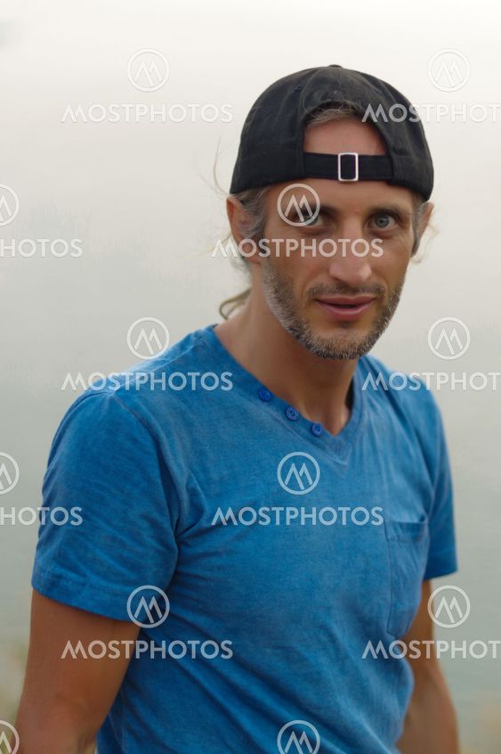 Happy Young Bearded Man sitting on view point with a seascape wearing in blank blue t-shirt and black Cap