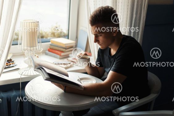 Handsome man drinking coffee and reads magazine in the...
