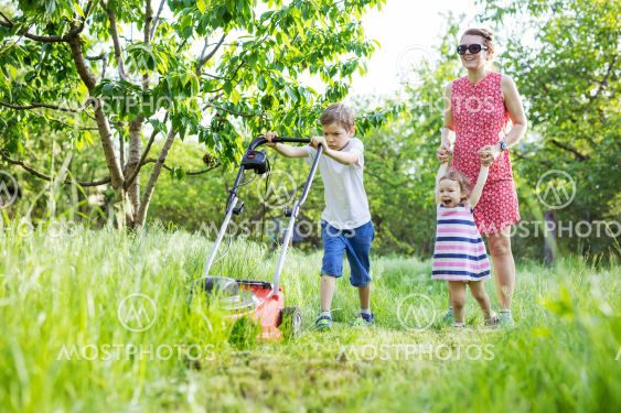 Young boy mowing grass with lawn mower, mother and...