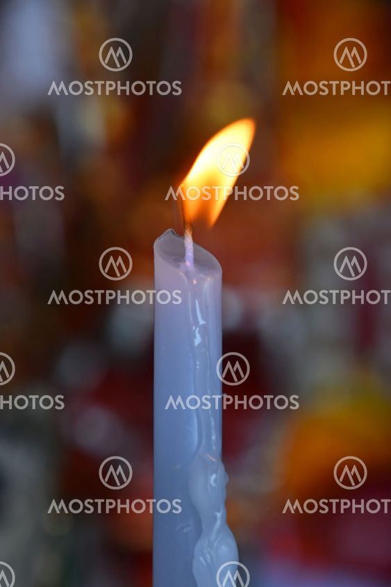 Flame of white melting candle in temple or church