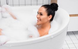 Young cheerful woman bathing with foam in bathtub