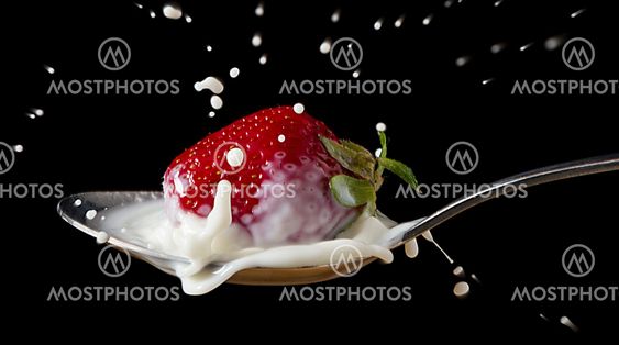 red, ripe strawberry falling in spoon with milk