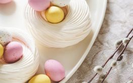 Easter meringue nests with colorful sweet eggs on plate.