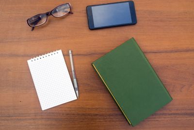 Book, notepad, pen, eyeglasses and smart phone on wooden...
