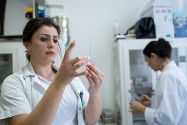 A focused nurse in a white lab coat carefully prepares a...