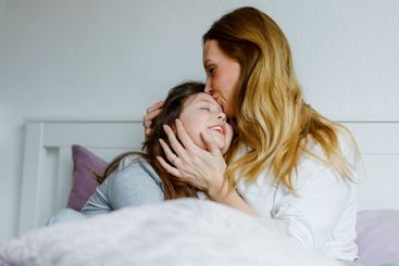 Lovely young mother and cute school kid girl cuddling...