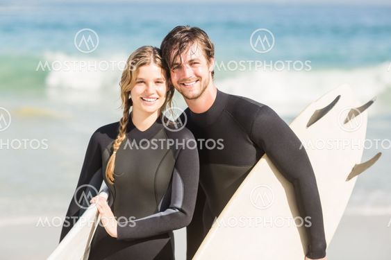 Portrait of couple with surfboard standing on the beach