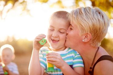 Kiss, blowing bubbles and child in park with mom for...