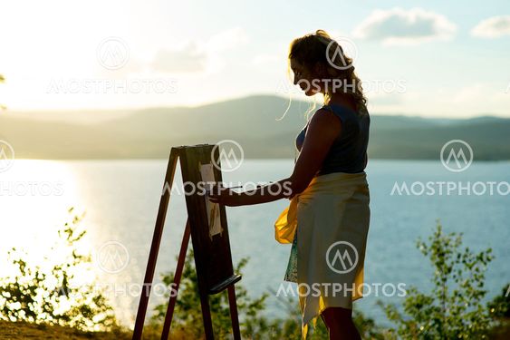 young artist draws a seascape at sunset