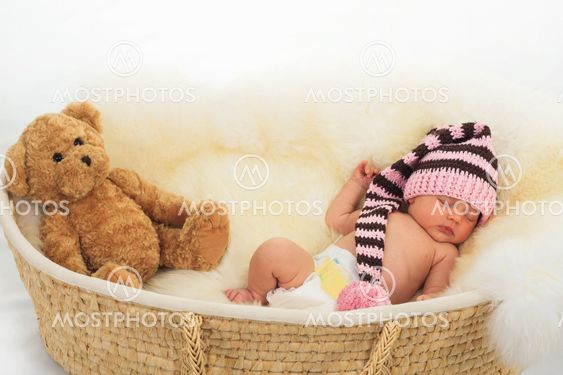 infant sleeping on a white sheepskin in a wicker basket.