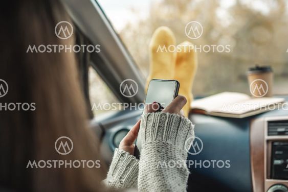 Woman in a car in warm socks is holding a mobile phone...