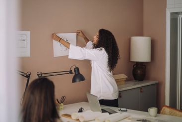 Side view of female architect sticking blueprint on wall...
