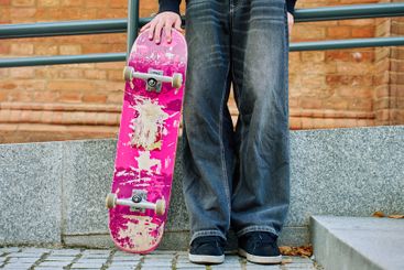 Skateboarder holding worn pink skateboard at street