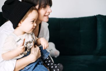 Mother and toddler wearing beanie sitting together on...