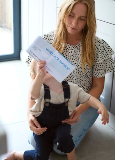 Mother Cuddling Son At Home With Letter About Increase...