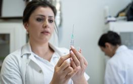 A focused nurse in a white lab coat carefully prepares a...