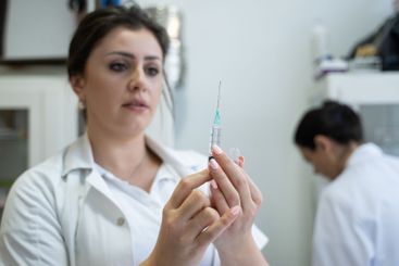 A focused nurse in a white lab coat carefully prepares a...