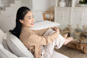 Happy dreamy beautiful Asian woman relaxing on soft couch