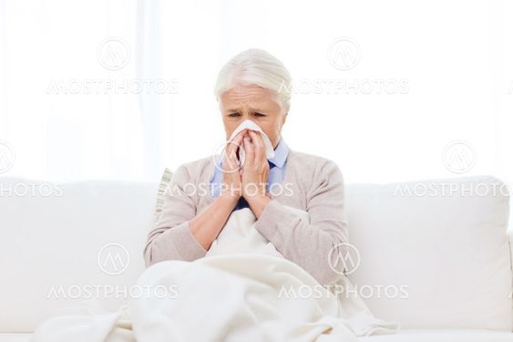 sick senior woman blowing nose to paper napkin