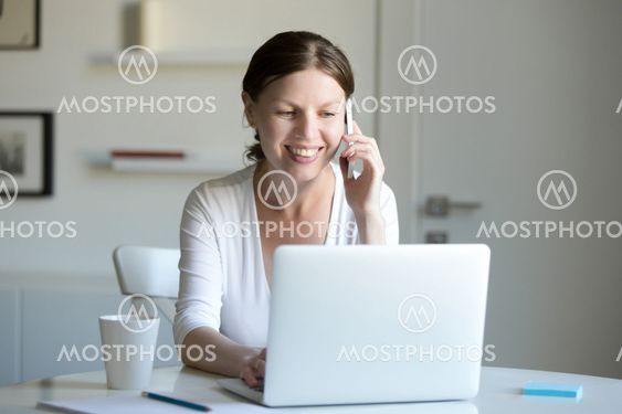 Portrait of smiling woman near laptop talking on the phone.