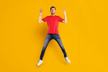Happy guy jumping over blue studio wall