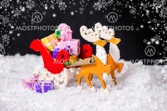 beautiful composition of Christmas decoration reindeer and Santa sleigh with gifts in snow on black background, closeup
