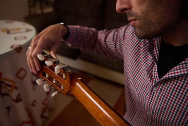 Man tuning a classical guitar in a cozy indoor setting