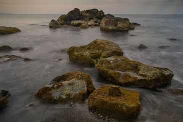 Rocky shoreline at dusk with gentle waves kissing the...