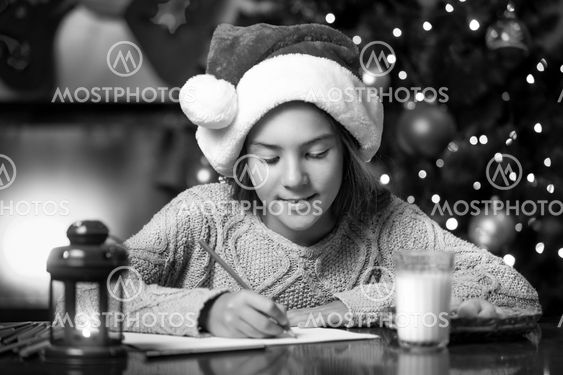 portrait of cute girl writing letter to Santa Claus at...