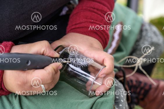hands of a woman engraving a decorative pattern into a...