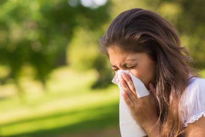 Woman blowing nose with tissue paper at park