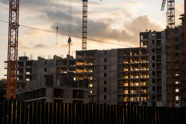 Cranes operate at dusk, lifting materials above a...