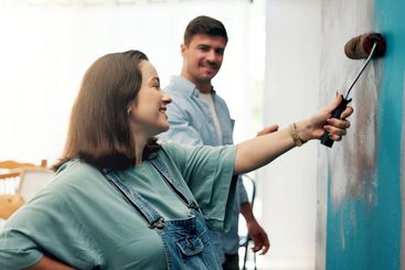 Couple, excited and painting a wall in home for diy...