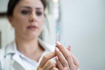 A focused nurse in a white lab coat carefully prepares a...