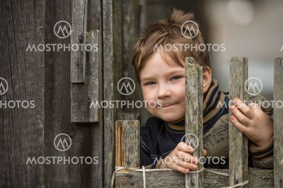 Portrait of little boy near a fence in the village.