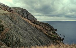 Coastal cliffs against a dramatic sky near a calm sea,...