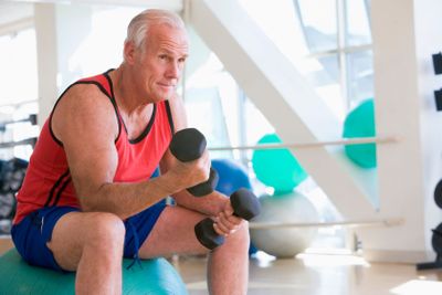 Man Using Hand Weights On Swiss Ball At Gym