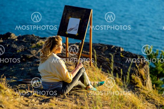 young artist draws a seascape at sunset