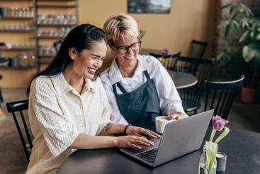 Happy female owner working on laptop while sitting with...