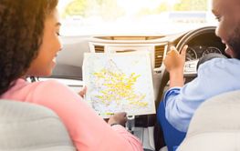 Happy black couple looking at paper map sitting inside car