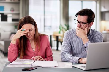 Young couple sitting in kitchen stressed about financial...