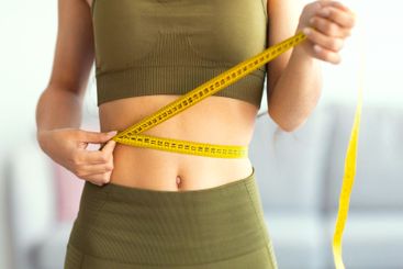 Cropped view of slim Indian woman measuring her waist...