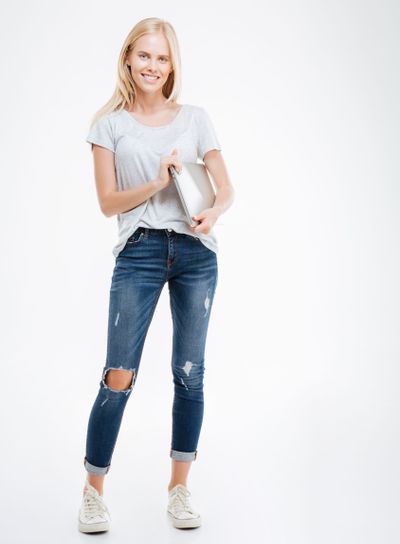 Full length portrait of a casual woman standing with laptop
